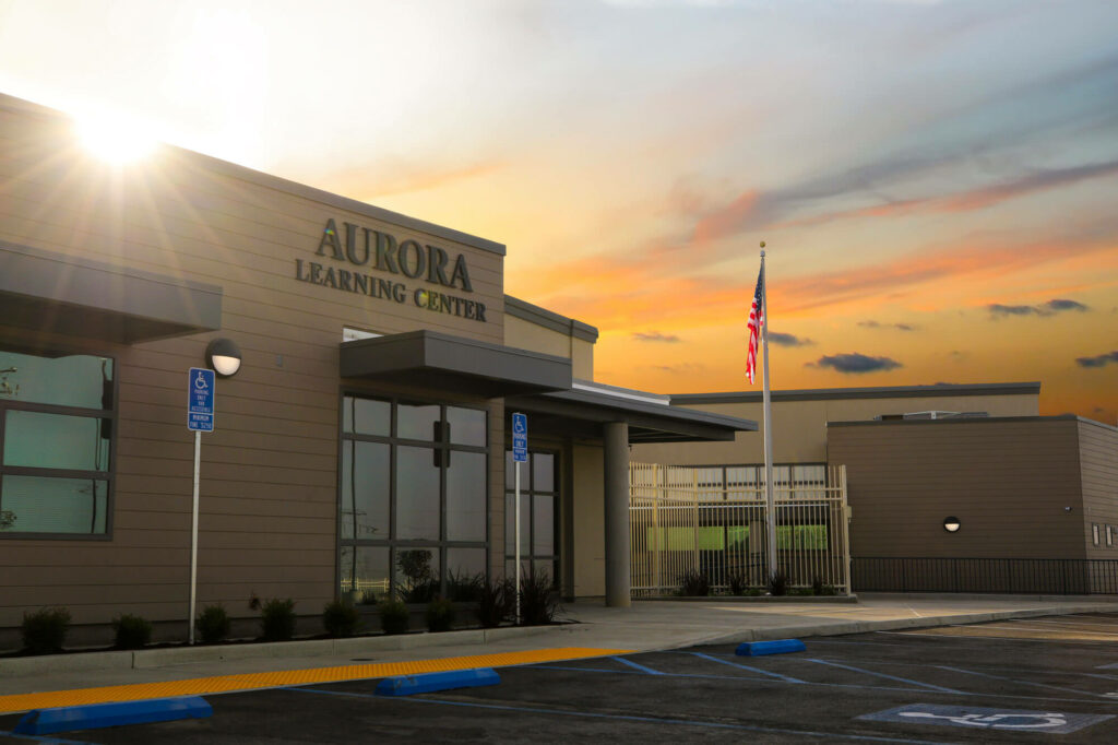 Mid-shot of the front of the Aurora Learning Center building with a orange sunset in the sky behind it.